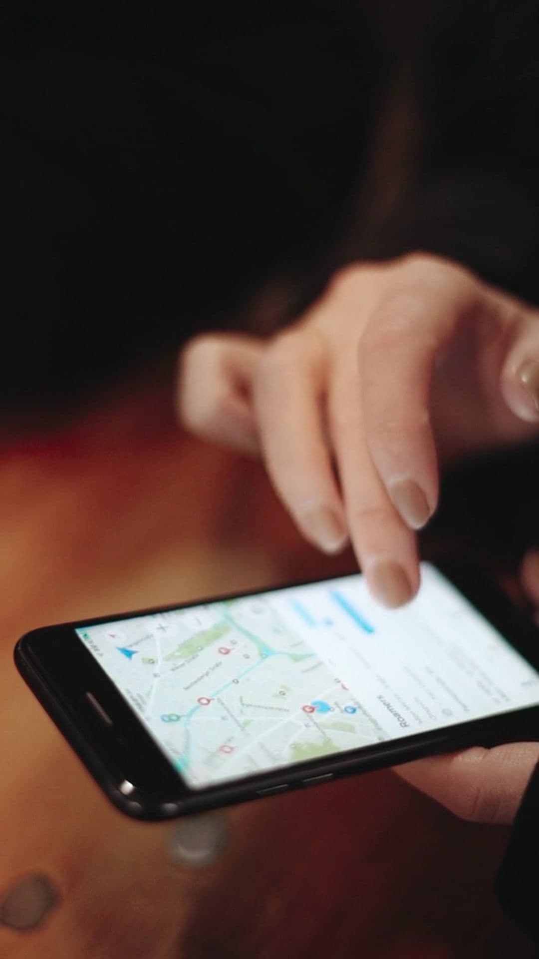 A hand reaching to a phone showing a map on a table.